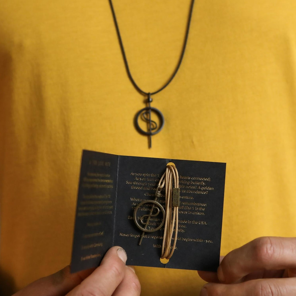 A model wearing the 108 Talisman Necklace in Ceramic Black while holding the 108 card and Antique Gold Necklace.