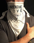 A man wearing the Artist Collab: Gem & Bolt x One Golden Thread Versawrap as a face covering with the message "Breathe Love" in white color