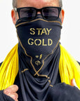 A man wearing the Artist Collab: Gem & Bolt x One Golden Thread Versawrap as a face covering with the message "Stay Gold" in black color