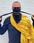 A man wearing the Artist Collab: Gem & Bolt x One Golden Thread Versawrap as a face covering with the message "Breathe Love" in black color