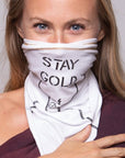 A woman wearing the Artist Collab: Gem & Bolt x One Golden Thread Versawrap as a face covering with the message "Stay Gold" in white color