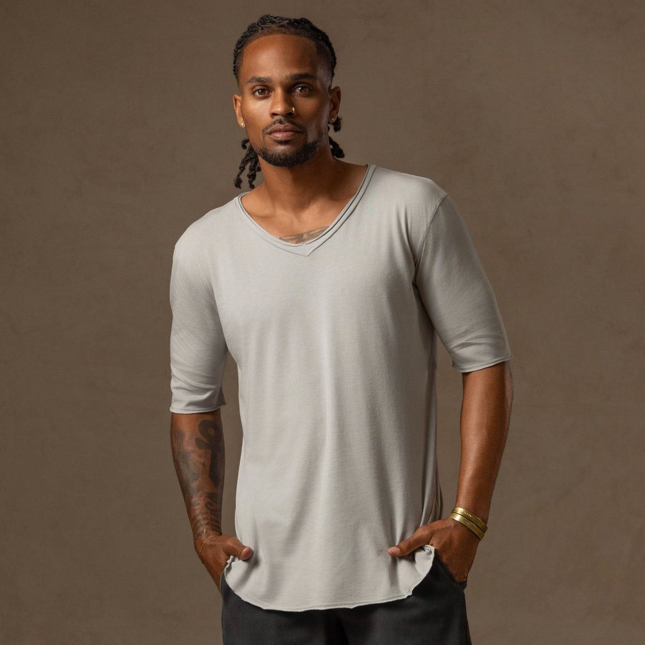 Man with curly hair wearing a loose, dark shirt poses against a plain gray background.