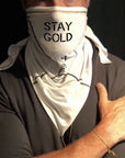 A man wearing the Artist Collab: Gem & Bolt x One Golden Thread Versawrap as a face covering with the message "Stay Gold" in white color