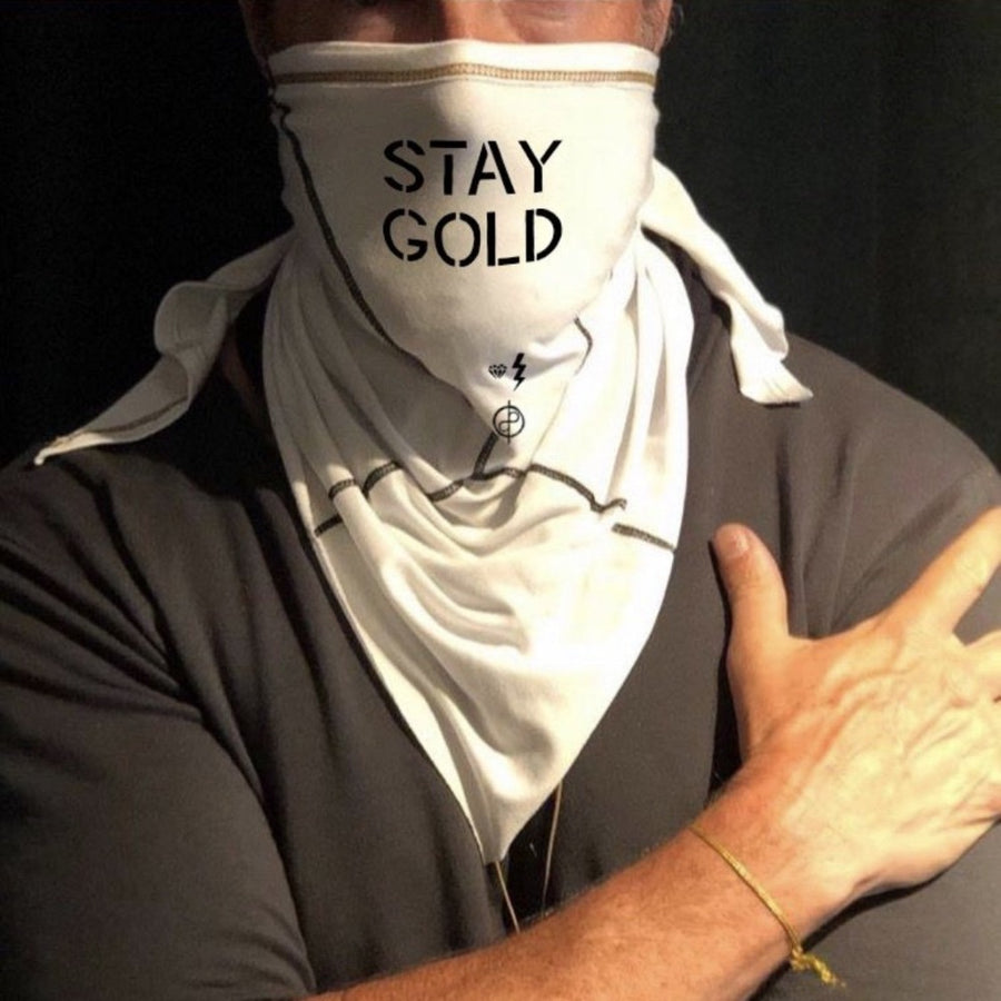 A man wearing the Artist Collab: Gem & Bolt x One Golden Thread Versawrap as a face covering with the message "Stay Gold" in white color