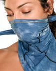 A woman wearing the One Golden Thread Versawrap as a face covering in Desert Blue TieDye color