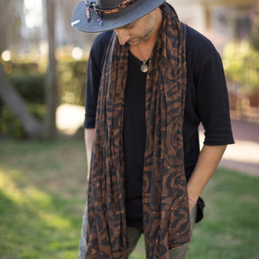 A man wearing the Artist Collab: Daniel Dugan x One Golden Thread Nature Wrap as a scarf in Egyptian Tan color