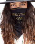 A woman wearing the One Golden Thread Versawrap as a face covering with the message "Breathe Love" in Black color