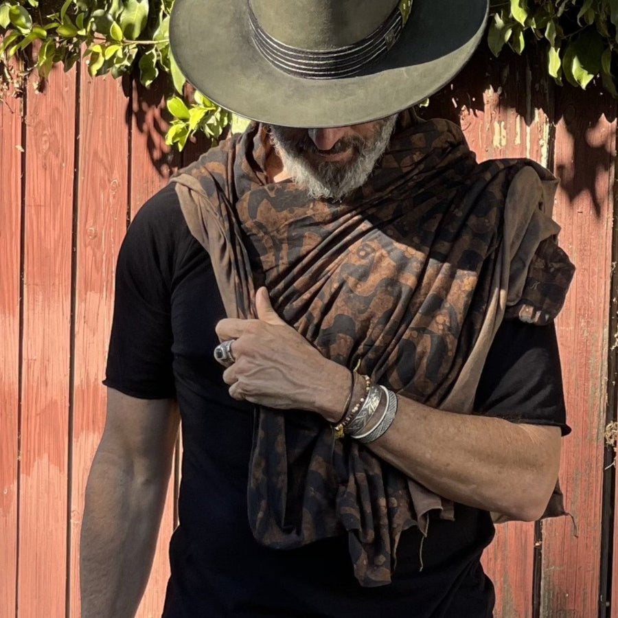 A man wearing the Artist Collab: Daniel Dugan x One Golden Thread Nature Wrap as a scarf in Egyptian Tan color