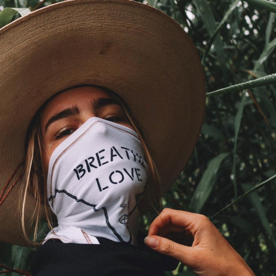 A woman wearing the One Golden Thread Versawrap as a face covering with the message "Breathe Love" in white color
